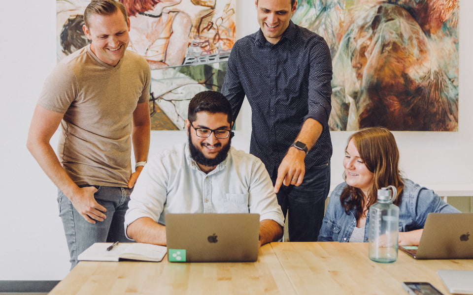 Four people looking at computer screen smiling